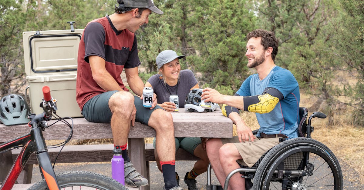 Group of friends having fun outdoors, chatting and enjoying drinks by a picnic table.