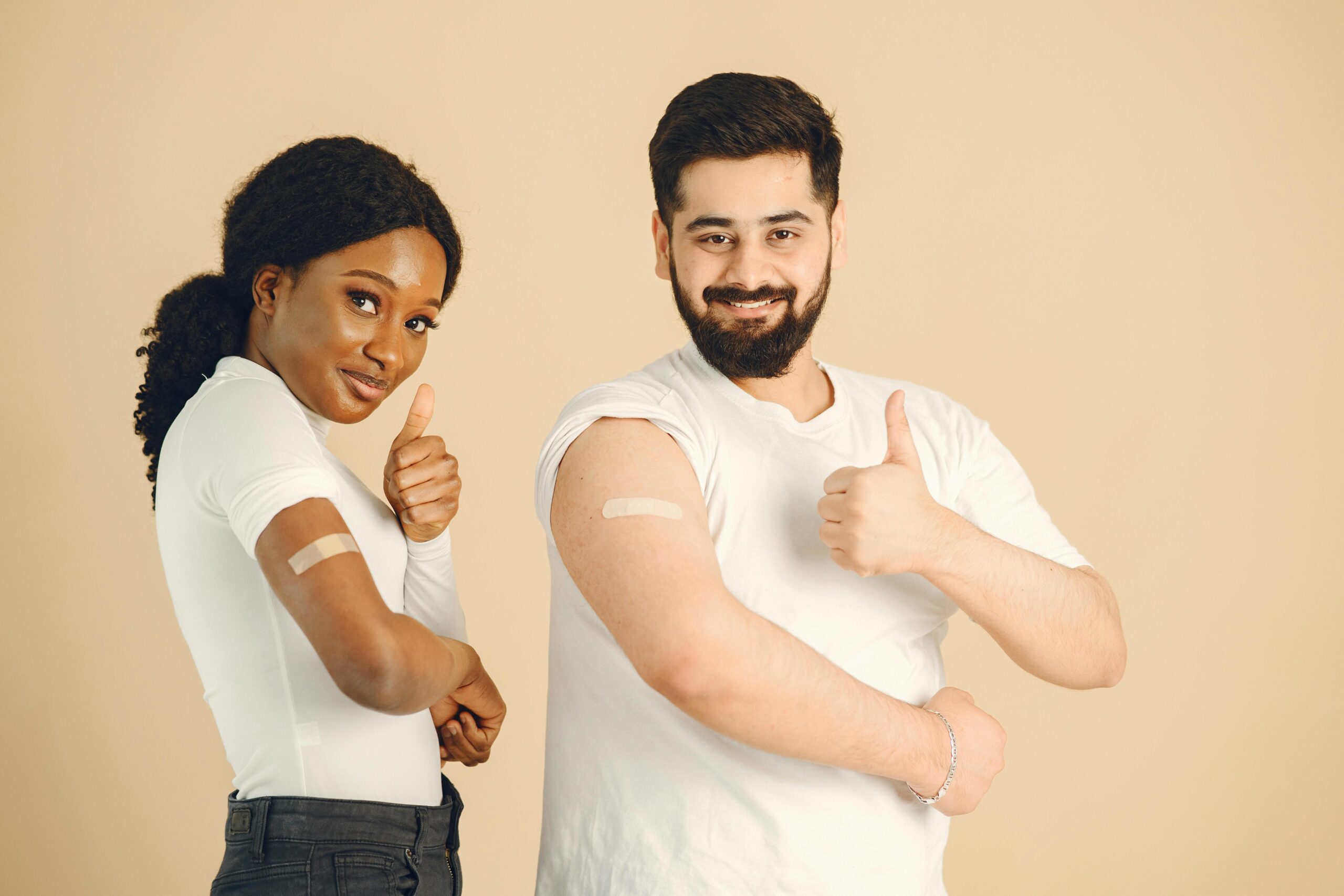 Two people showing band-aids and thumbs up after vaccination. Positive health concept.